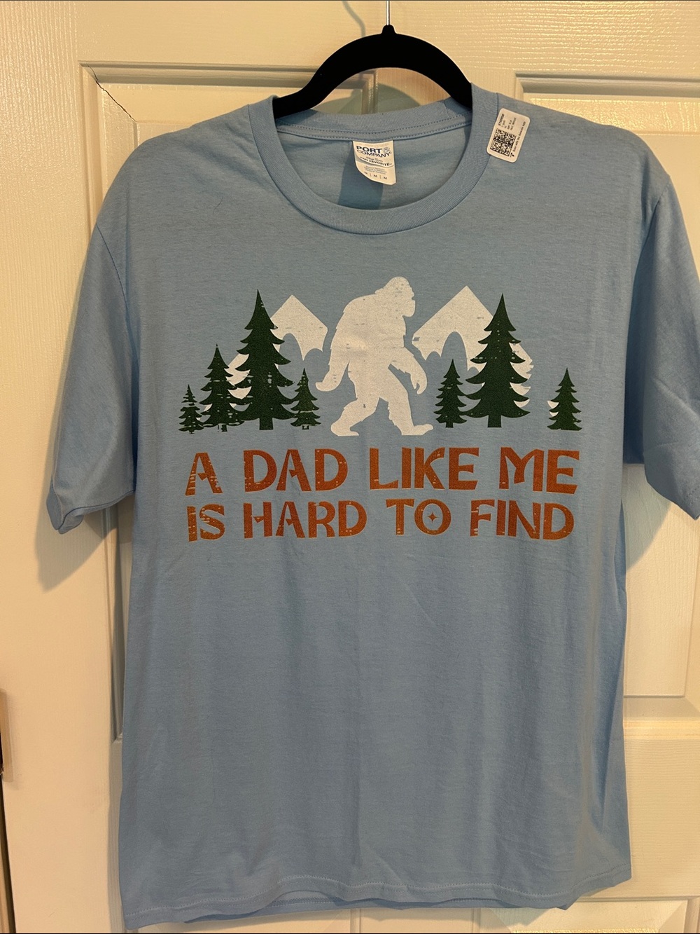 Men’s Port & Company Light Blue Bigfoot Graphic Tee w/Green Trees & Orange Text
